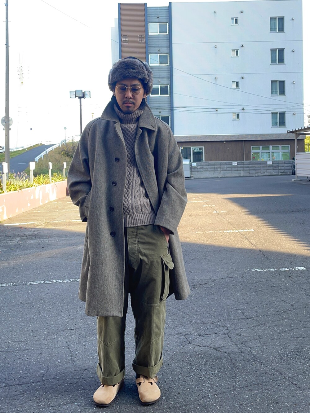 ベージュ系のニット/セーター、ベージュ系のサンダル、グレー系のステンカラーコートを着用したメンズの秋コーディネートの2枚目の写真