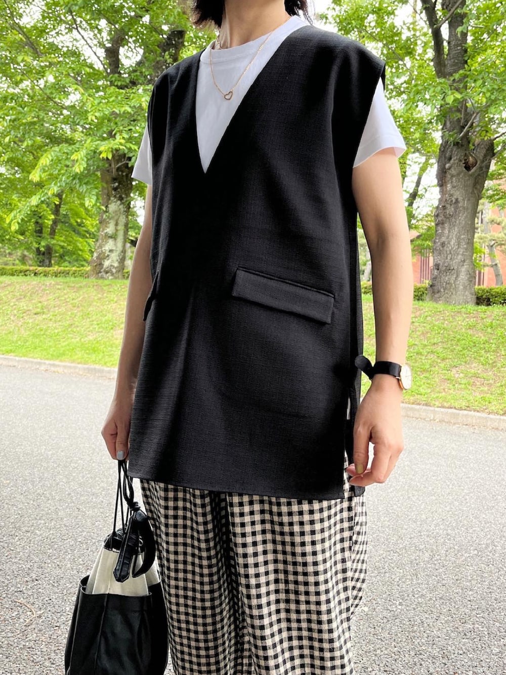 ブラック系のベスト、ホワイト系のパンツ、ブラック系のサンダルを着用したレディースの春コーディネートの2枚目の写真