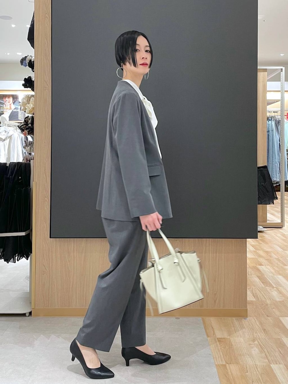 ホワイト系のショルダーバッグ、ブラック系のパンプス、グレー系のスラックスを着用したレディースの冬コーディネートの2枚目の写真