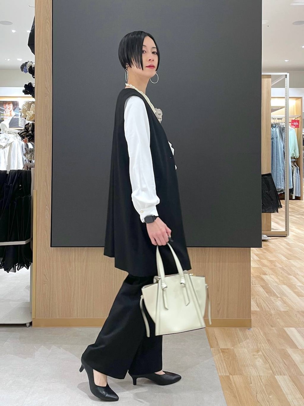 ホワイト系のショルダーバッグ、ブラック系のパンプス、ブラック系のスラックスを着用したレディースの冬コーディネートの2枚目の写真