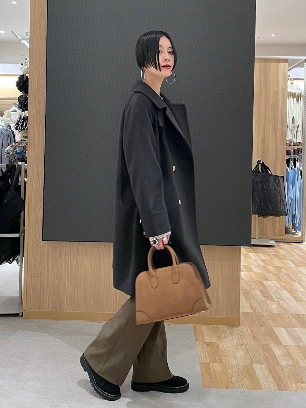 ブラック系のチェスターコート、ホワイト系のニット/セーター、ブラウン系のその他パンツを着用したレディースの冬コーディネートの2枚目の写真