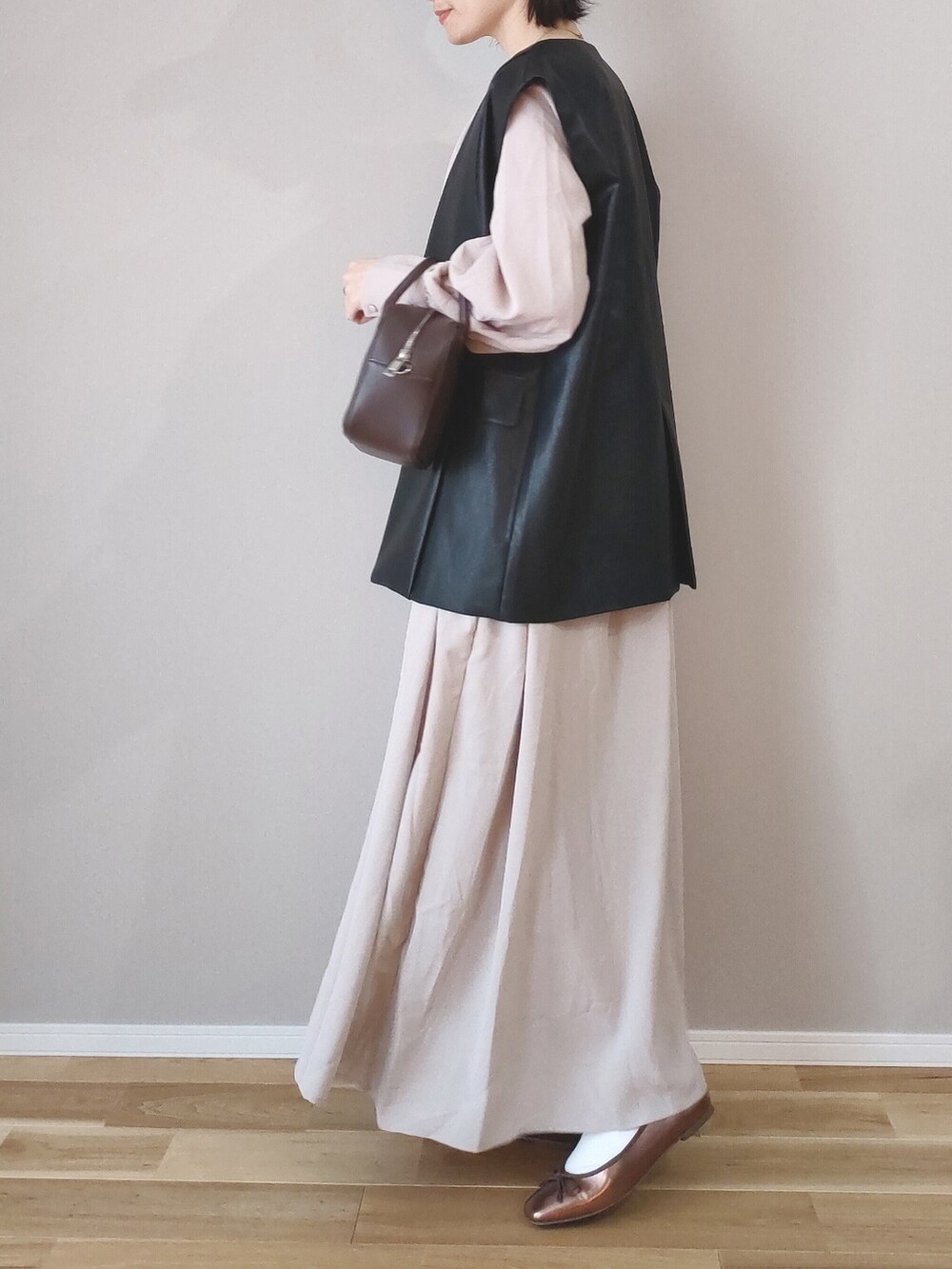 ベージュ系のワンピース、ブラック系のベスト、ブラウン系のボストンバッグを着用したレディースの春コーディネートの3枚目の写真