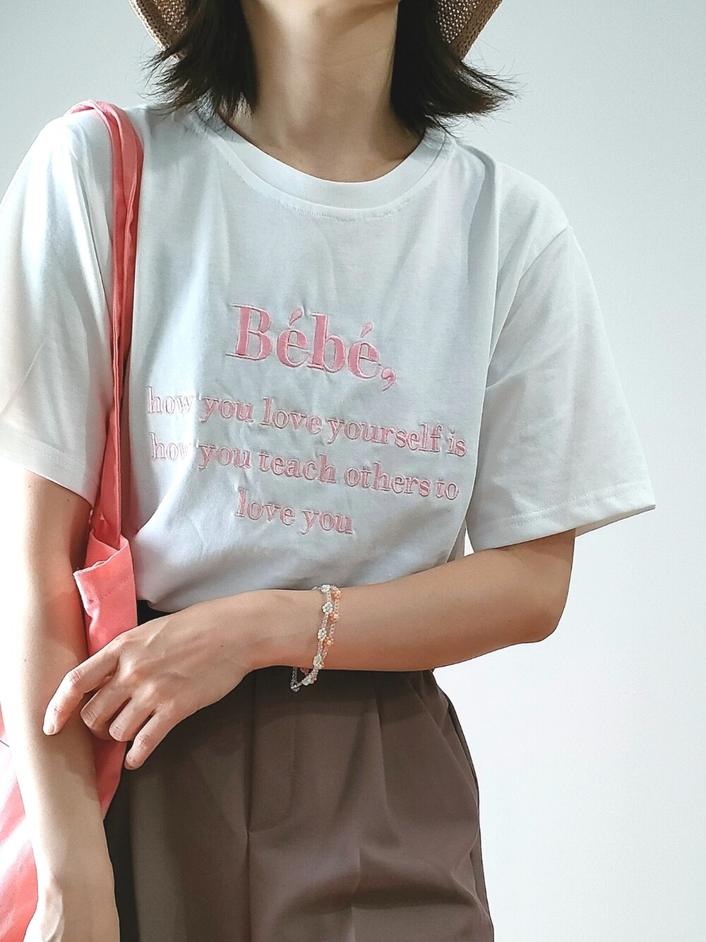 ホワイト系のTシャツ/カットソー、ブラウン系のスラックス、ピンク系のトートバッグを着用したレディースの夏コーディネートの3枚目の写真