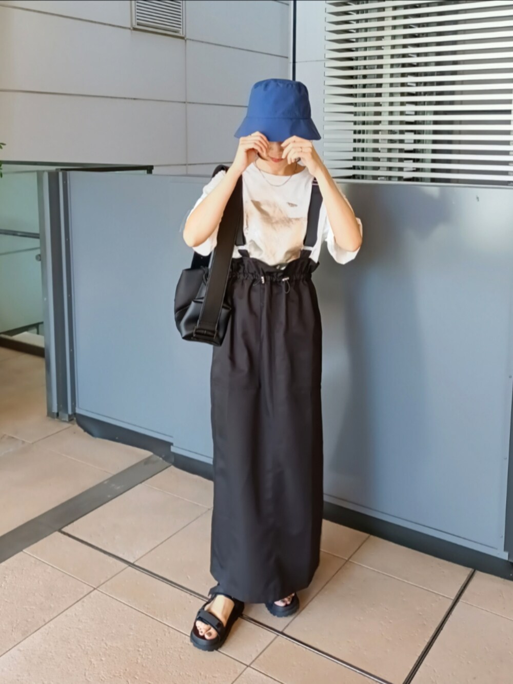 ブラック系のジャンパースカート、ホワイト系のTシャツ/カットソー、ブラック系のショルダーバッグを着用したレディースの夏コーディネートの2枚目の写真