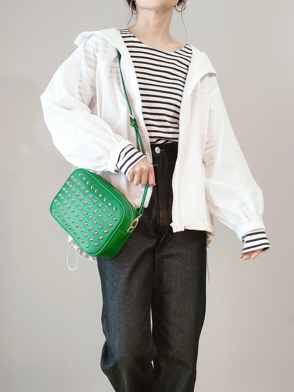 グリーン系のショルダーバッグ、ホワイト系のマウンテンパーカー、ブラック系のデニムパンツを着用したレディースの春コーディネートの2枚目の写真