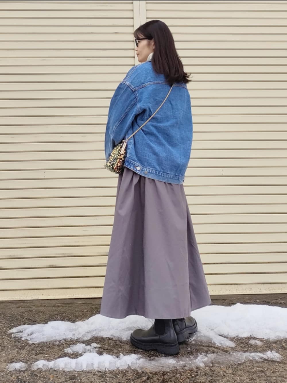 ブルー系のデニムジャケット、ホワイト系のワンピース、ゴールド系のハンドバッグを着用したレディースの冬コーディネートの5枚目の写真