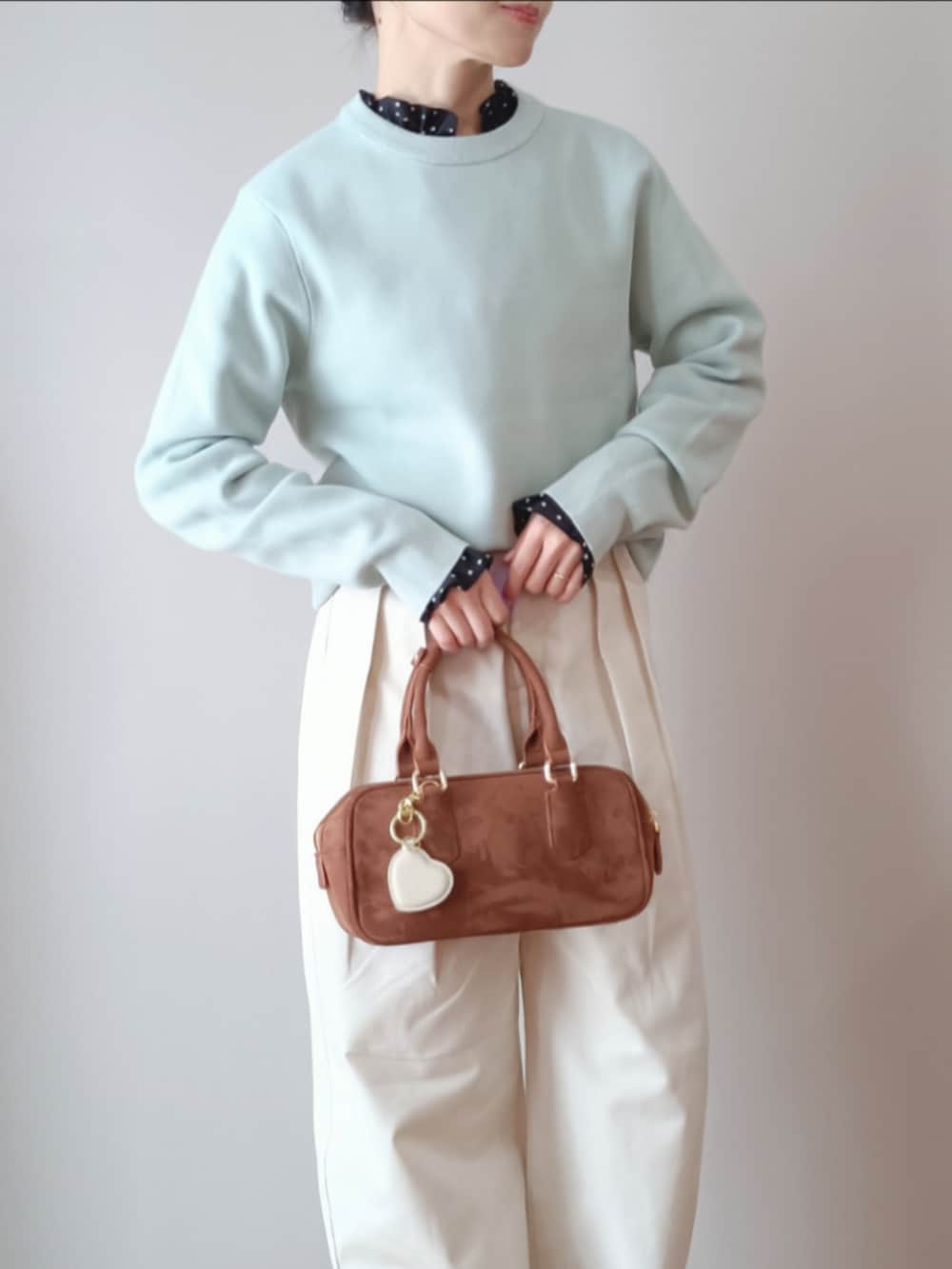 グリーン系のトップス、ホワイト系のチノパンツ、ブラウン系のボストンバッグを着用したレディースの春コーディネートの2枚目の写真