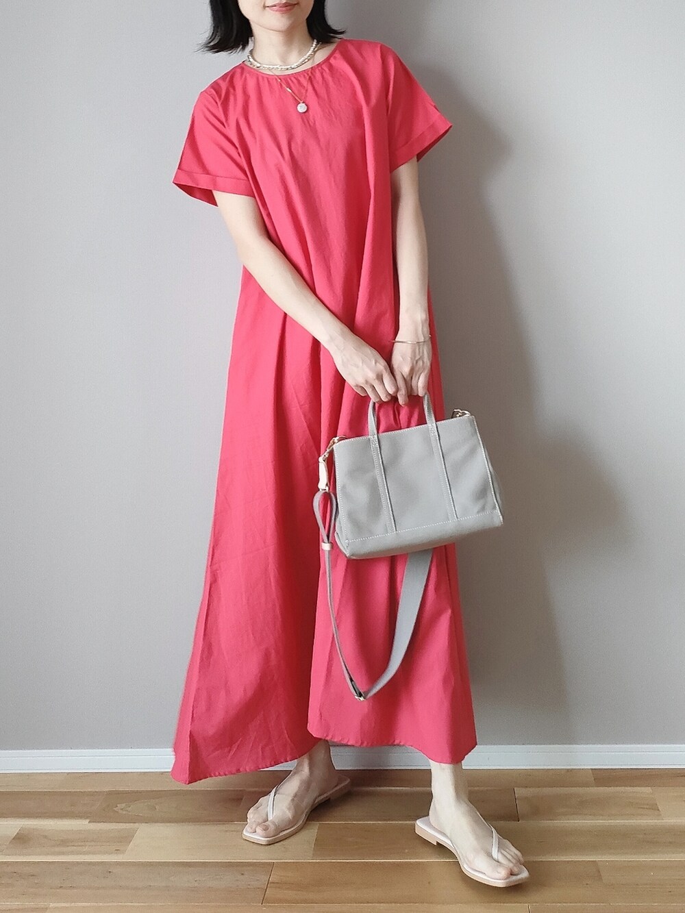 レッド系のワンピース、グレー系のハンドバッグ、ホワイト系のサンダルを着用したレディースの夏コーディネートの2枚目の写真
