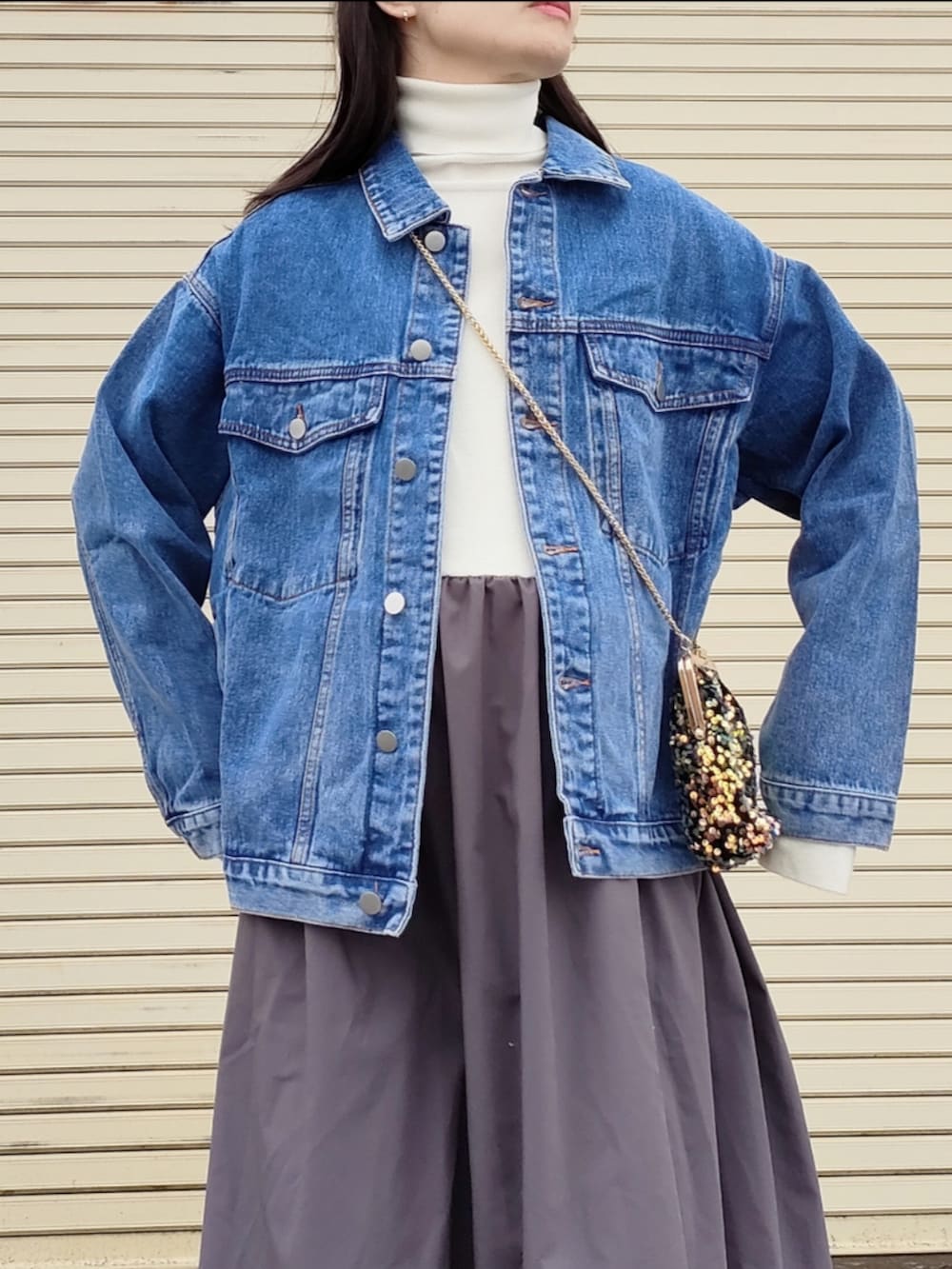 ブルー系のデニムジャケット、ホワイト系のワンピース、ゴールド系のハンドバッグを着用したレディースの冬コーディネートの2枚目の写真