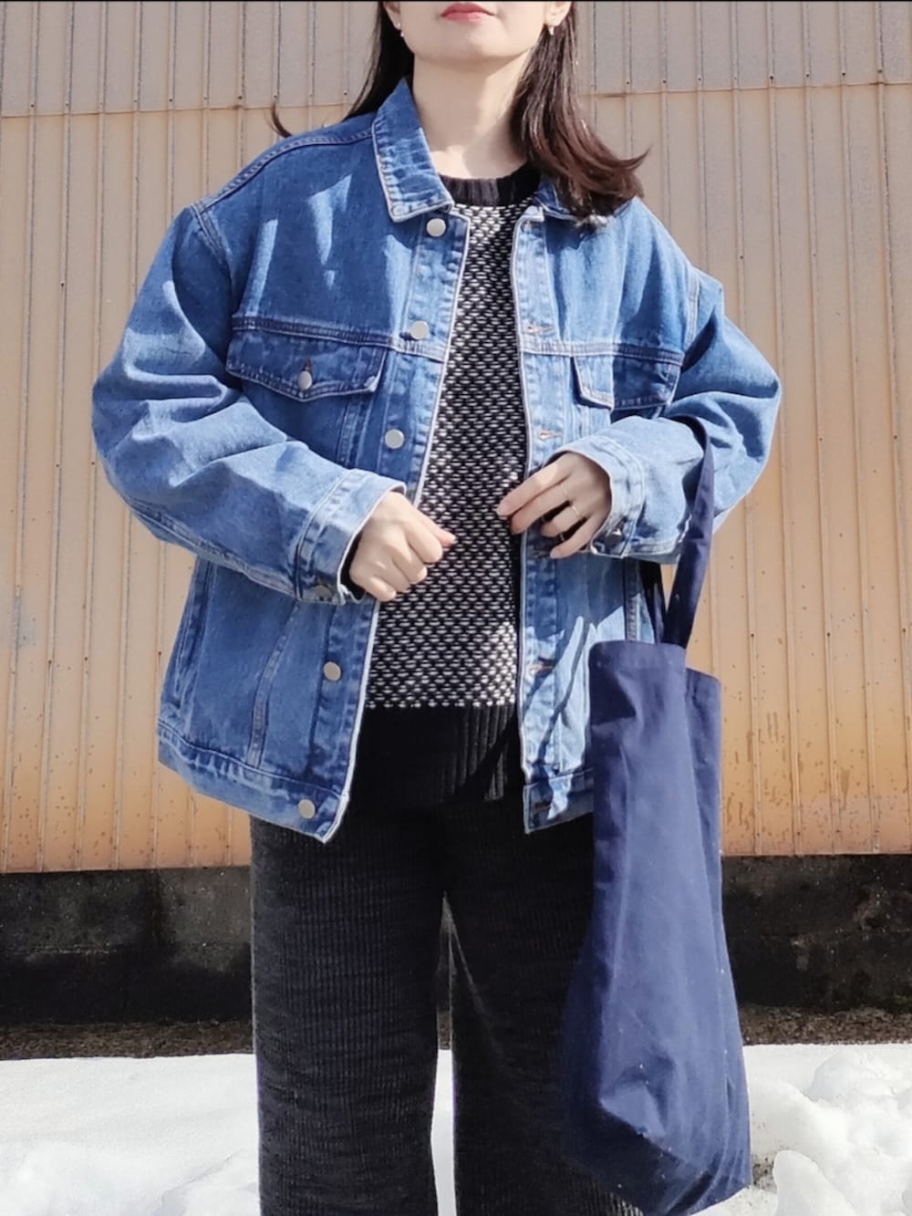 ブルー系のデニムジャケット、ブラック系のニット/セーター、ブルー系のトートバッグを着用したレディースの春コーディネートの2枚目の写真