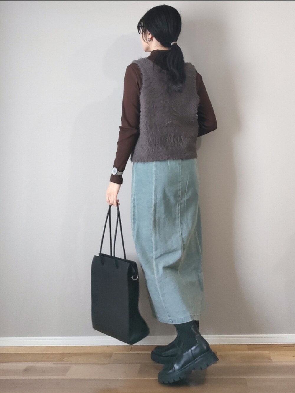 ブラック系のスカート、グレー系のベスト、ブラック系のブーツを着用したレディースの冬コーディネートの2枚目の写真