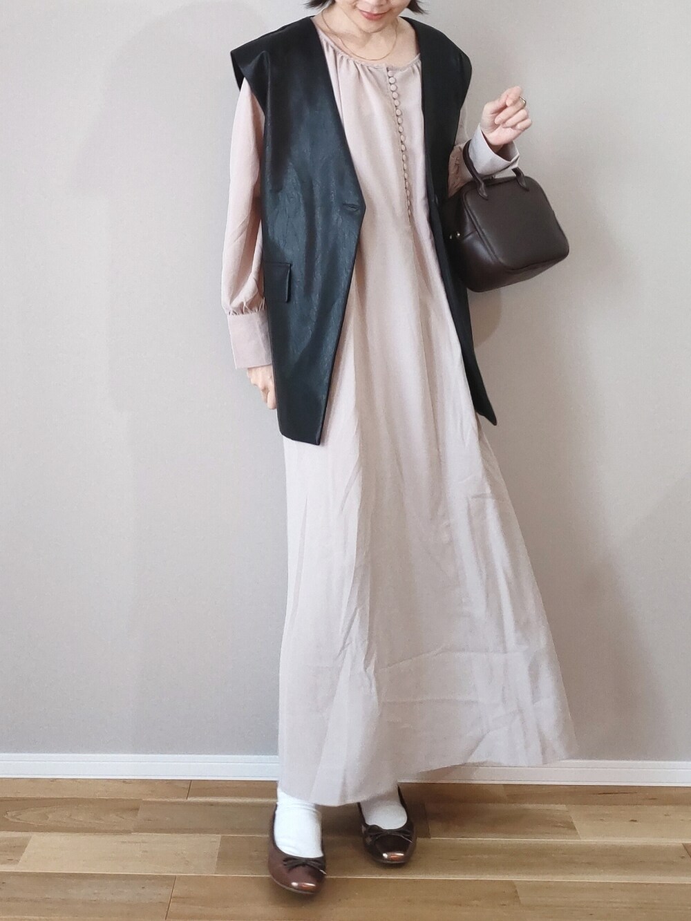 ベージュ系のワンピース、ブラック系のベスト、ブラウン系のボストンバッグを着用したレディースの春コーディネートの2枚目の写真