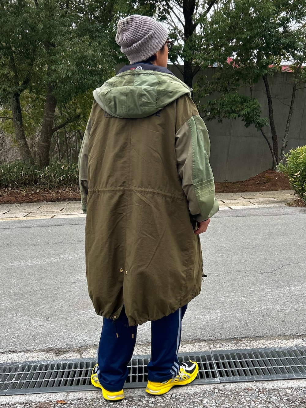 オレンジ系のベスト、グリーン系のモッズコート、ブルー系のスウェットパンツを着用したメンズの春コーディネートの4枚目の写真