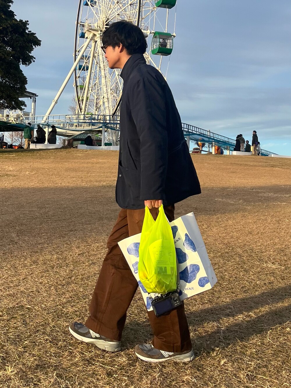 ブルー系のスニーカー、ブラウン系のチノパンツ、イエロー系のエコバッグ/サブバッグを着用したメンズの春コーディネートの2枚目の写真