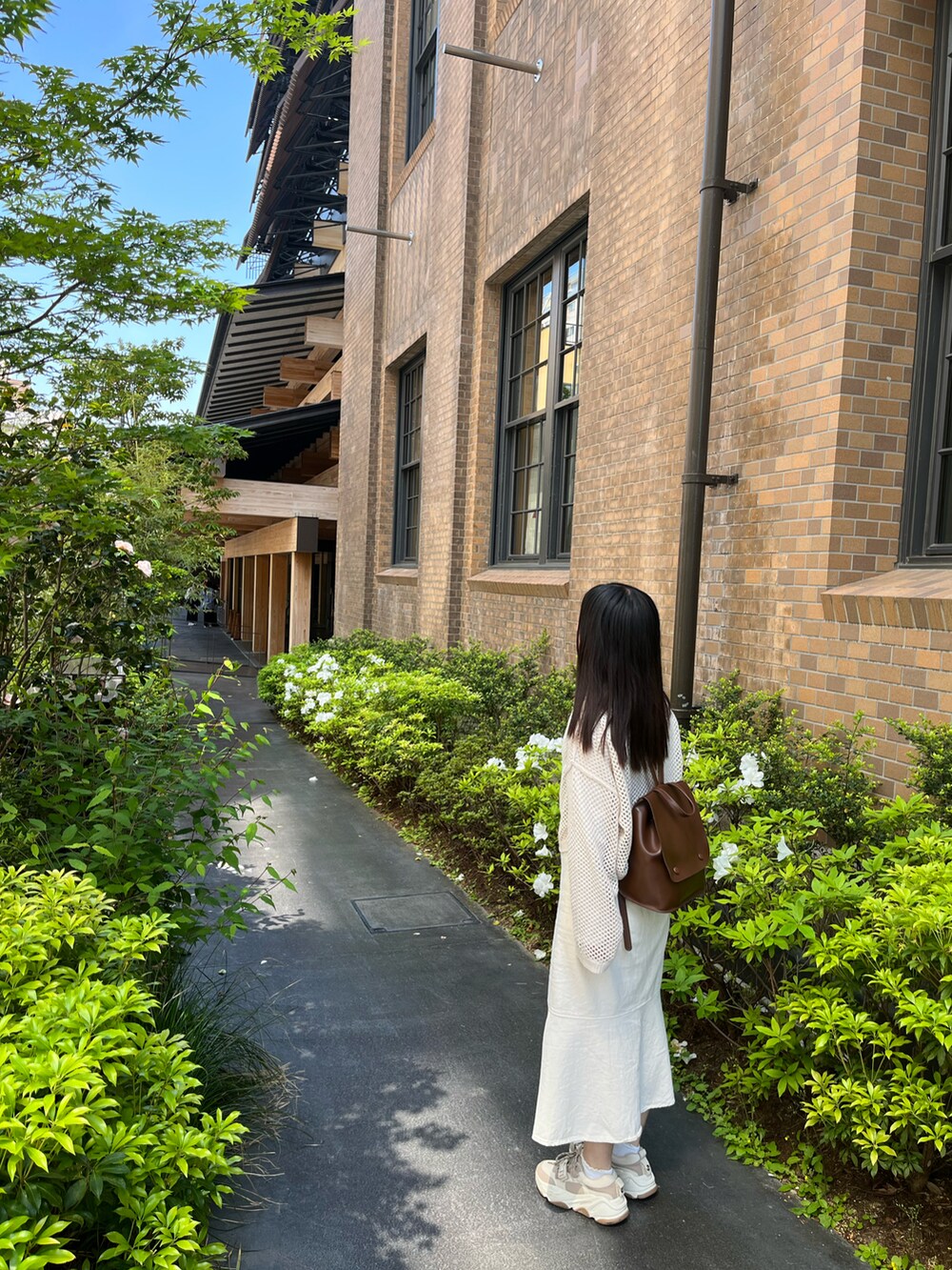 ベージュ系のトップス、ホワイト系のスカート、ベージュ系のスニーカーを着用したレディースの春コーディネートの2枚目の写真