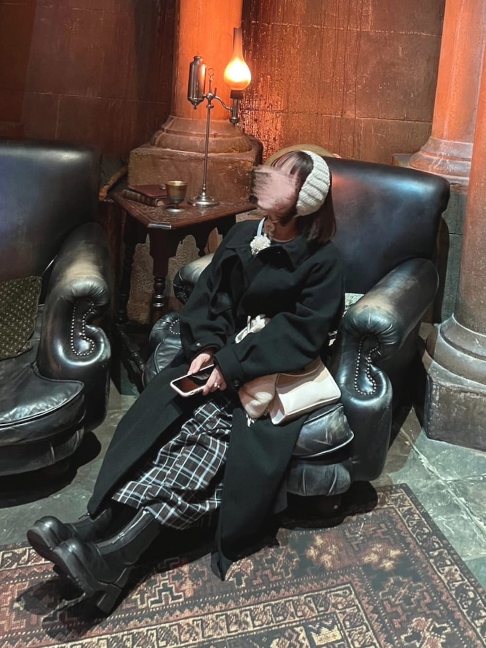 ブラック系のステンカラーコート、ブルー系のニット/セーター、ブラック系のブーツを着用したレディースの冬コーディネートの2枚目の写真