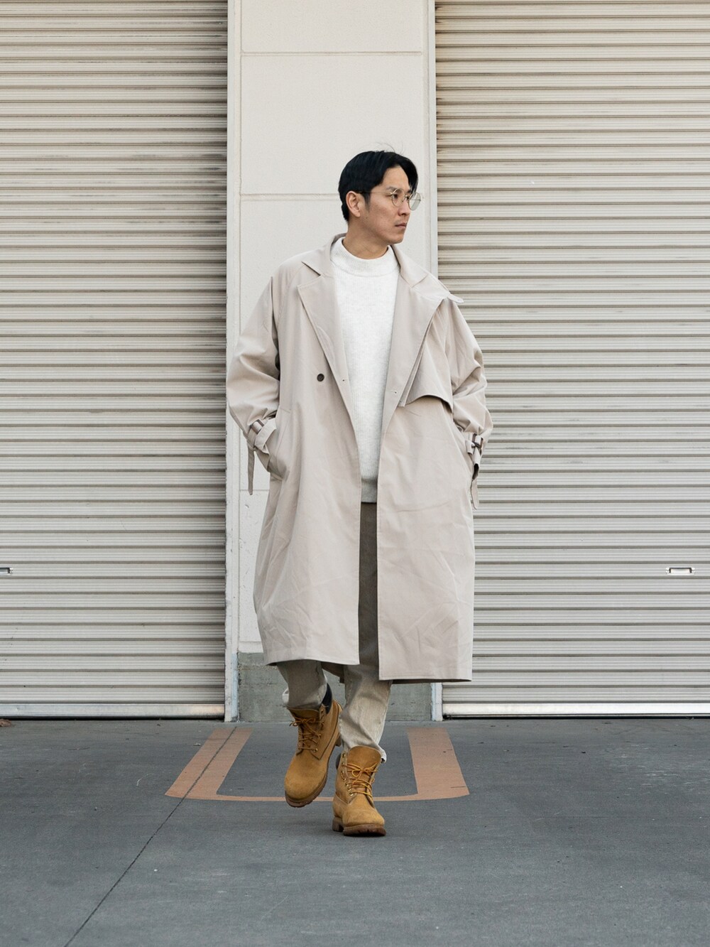 イエロー系のブーツ、ベージュ系のトレンチコート、ホワイト系のトップスを着用したメンズの冬コーディネートの2枚目の写真