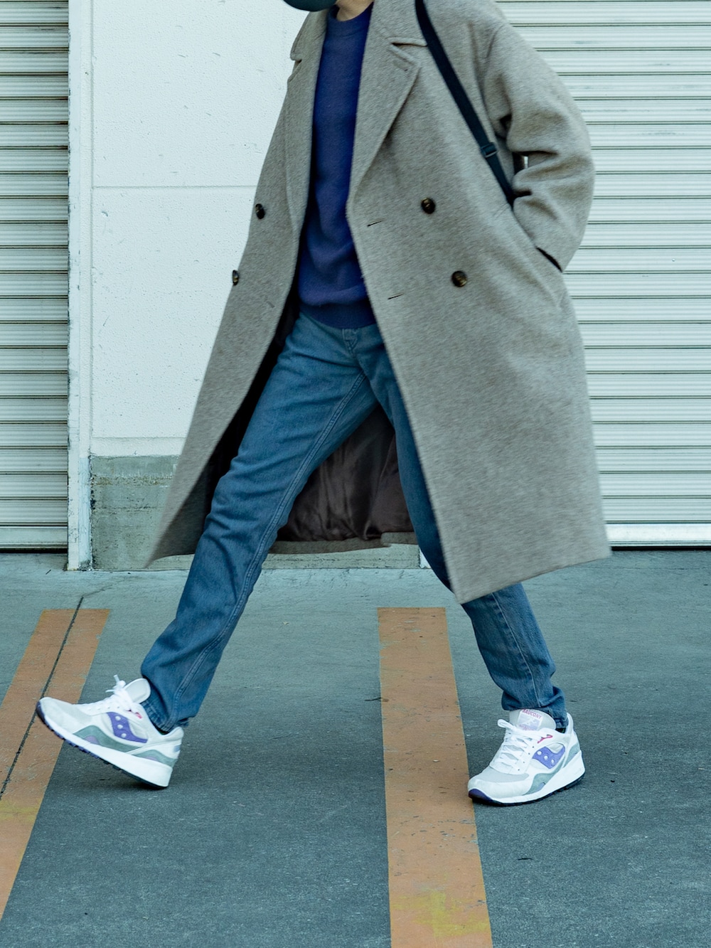 ベージュ系のステンカラーコート、ブルー系のデニムパンツ、ホワイト系のスニーカーを着用したメンズの冬コーディネートの2枚目の写真