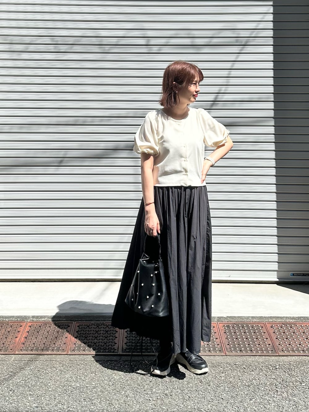 ホワイト系のトップス、ブラック系のスカート、ブラック系のハンドバッグを着用したレディースの夏コーディネートの2枚目の写真