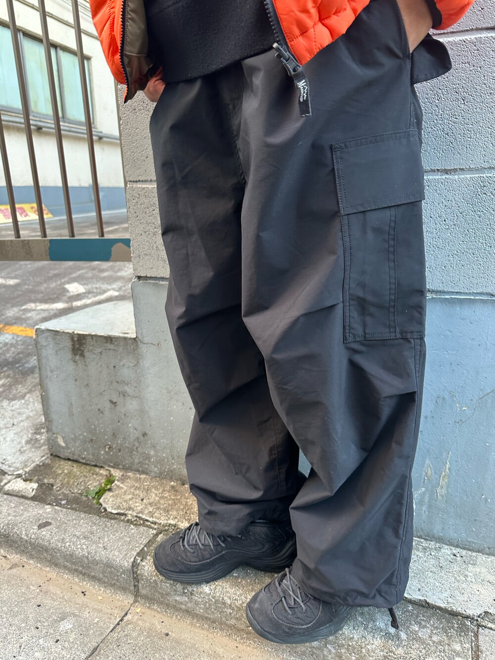 オレンジ系のマウンテンパーカー、ブラック系のカーゴパンツ、ブラック系のニット/セーターを着用したメンズの冬コーディネートの4枚目の写真
