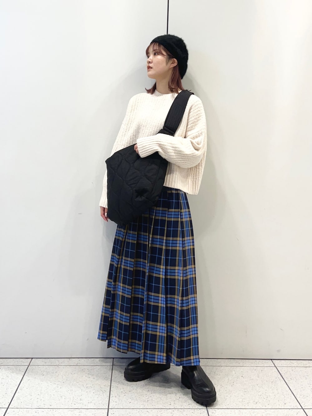 ブラック系のショルダーバッグ、ブルー系のスカート、ブラック系のブーツを着用したレディースの秋コーディネートの2枚目の写真