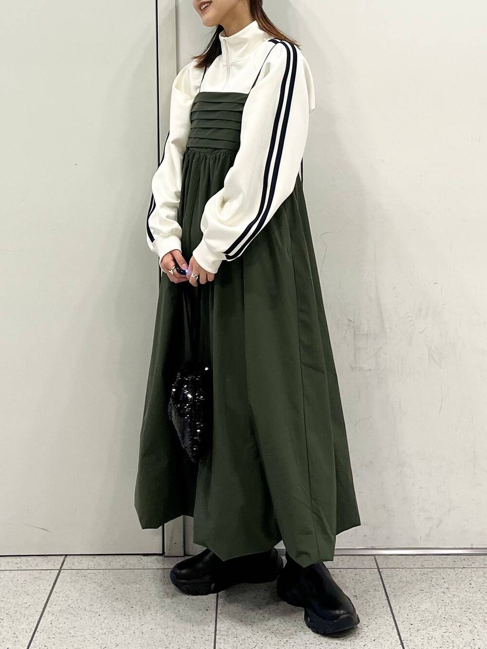 ブラック系のハンドバッグ、グリーン系のワンピース、ブラック系のブーツを着用したレディースの冬コーディネートの2枚目の写真