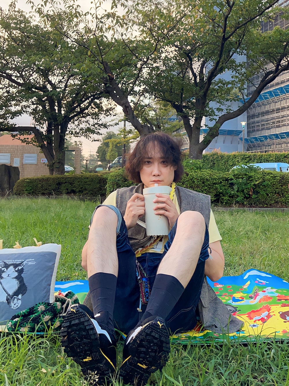 イエロー系のTシャツ/カットソー、ベージュ系のベスト、ブラック系のトートバッグを着用したメンズの秋コーディネートの2枚目の写真