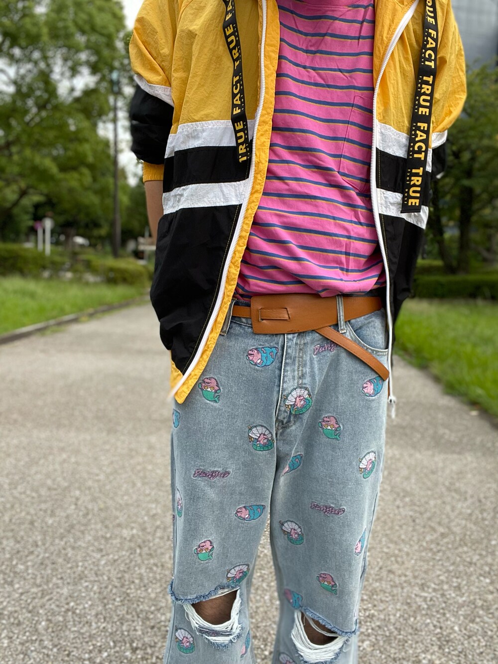 イエロー系のナイロンジャケット、ピンク系のTシャツ/カットソー、ブルー系のデニムパンツを着用したメンズの秋コーディネートの2枚目の写真