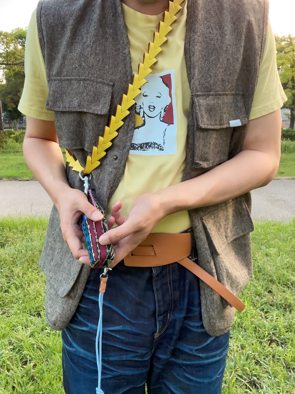 イエロー系のTシャツ/カットソー、ベージュ系のベスト、ブラック系のトートバッグを着用したメンズの秋コーディネートの4枚目の写真