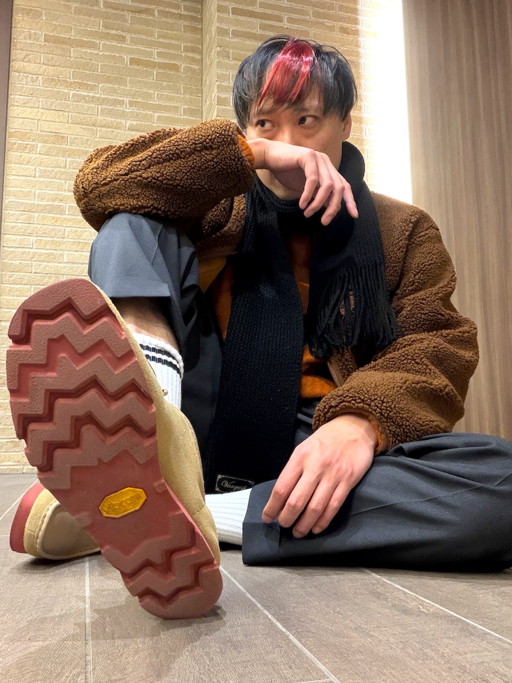 オレンジ系のニット/セーター、グレー系のスラックス、ブラウン系のその他アウターを着用したメンズの冬コーディネートの3枚目の写真