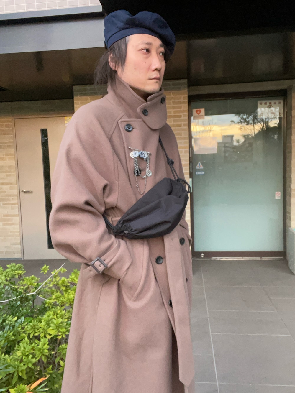 ベージュ系のトレンチコート、ブラック系のショルダーバッグ、ブルー系のスニーカーを着用したメンズの春コーディネートの2枚目の写真