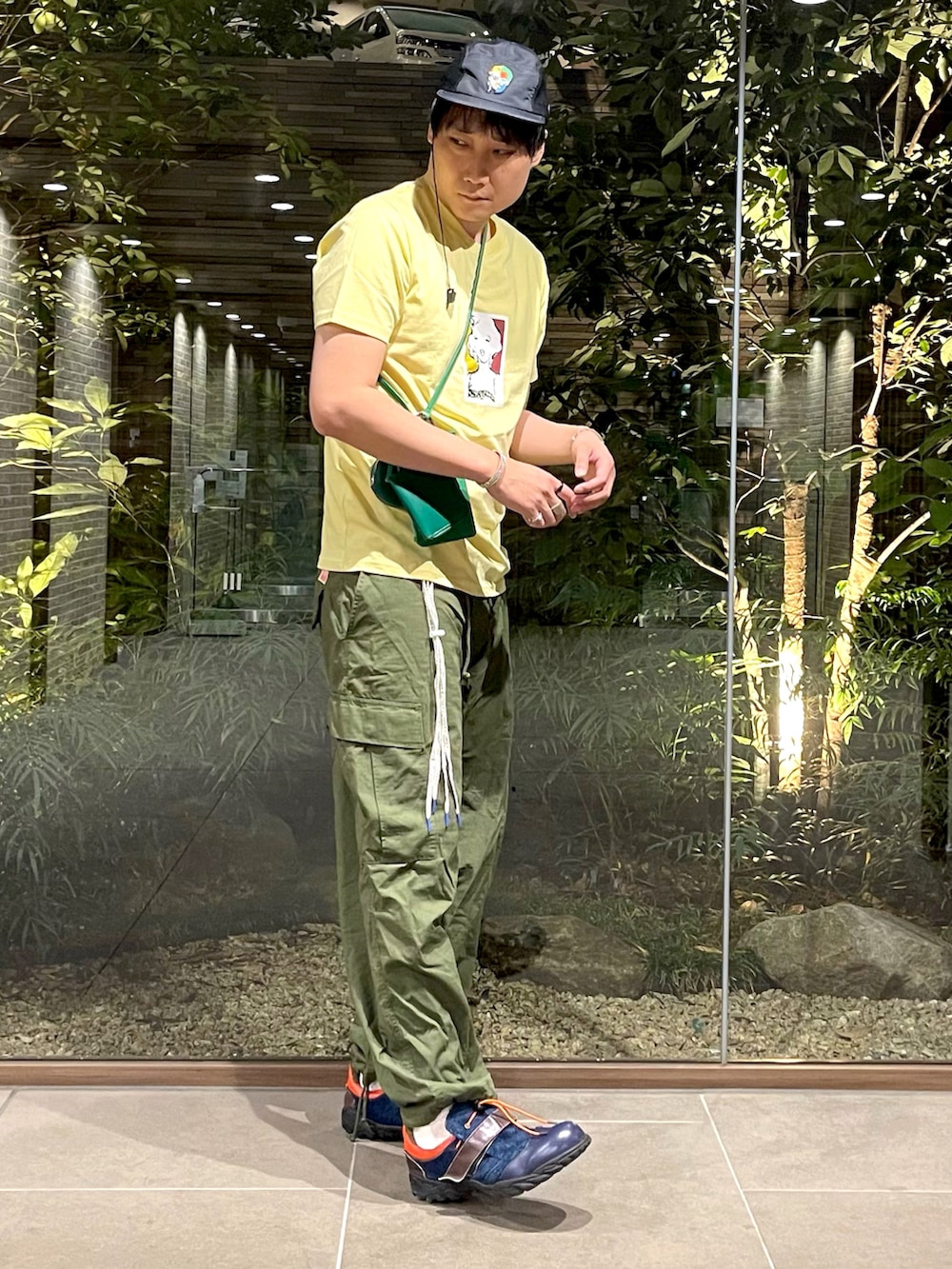 イエロー系のTシャツ/カットソー、グリーン系のショルダーバッグ、グリーン系のカーゴパンツを着用したメンズの夏コーディネートの2枚目の写真