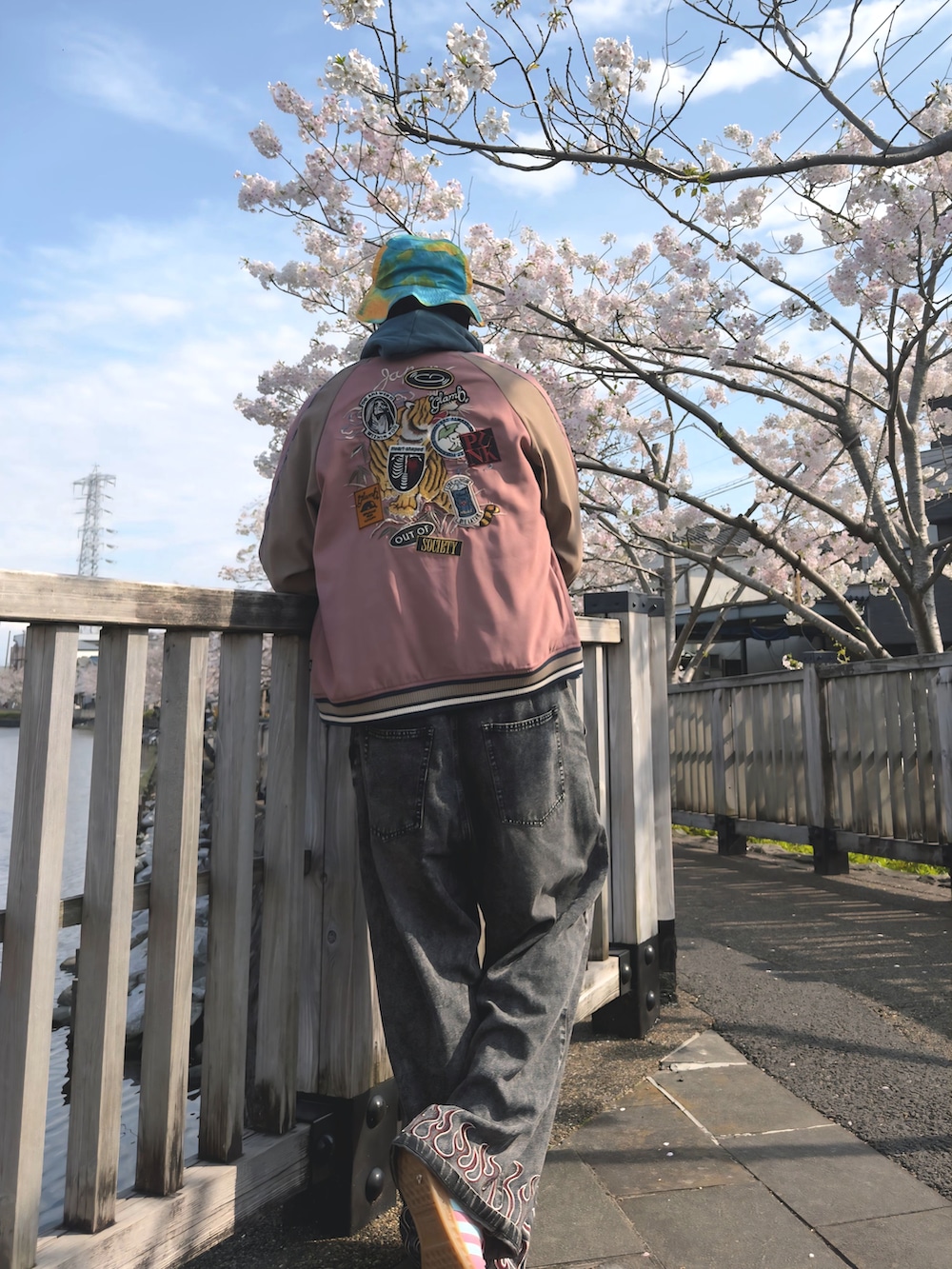 ブラック系のデニムパンツ、ブルー系のカーディガン/ボレロ、ピンク系のスカジャンを着用したメンズの春コーディネートの2枚目の写真