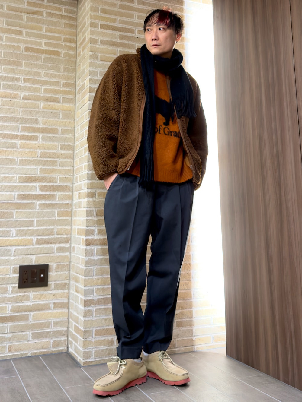 オレンジ系のニット/セーター、グレー系のスラックス、ブラウン系のその他アウターを着用したメンズの冬コーディネートの2枚目の写真