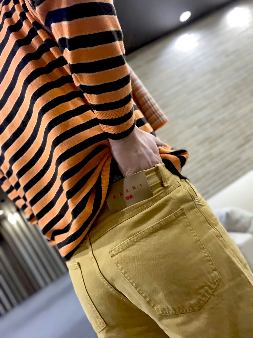 グレー系のTシャツ/カットソー、オレンジ系のニット/セーター、イエロー系のパンツを着用したメンズの冬コーディネートの3枚目の写真