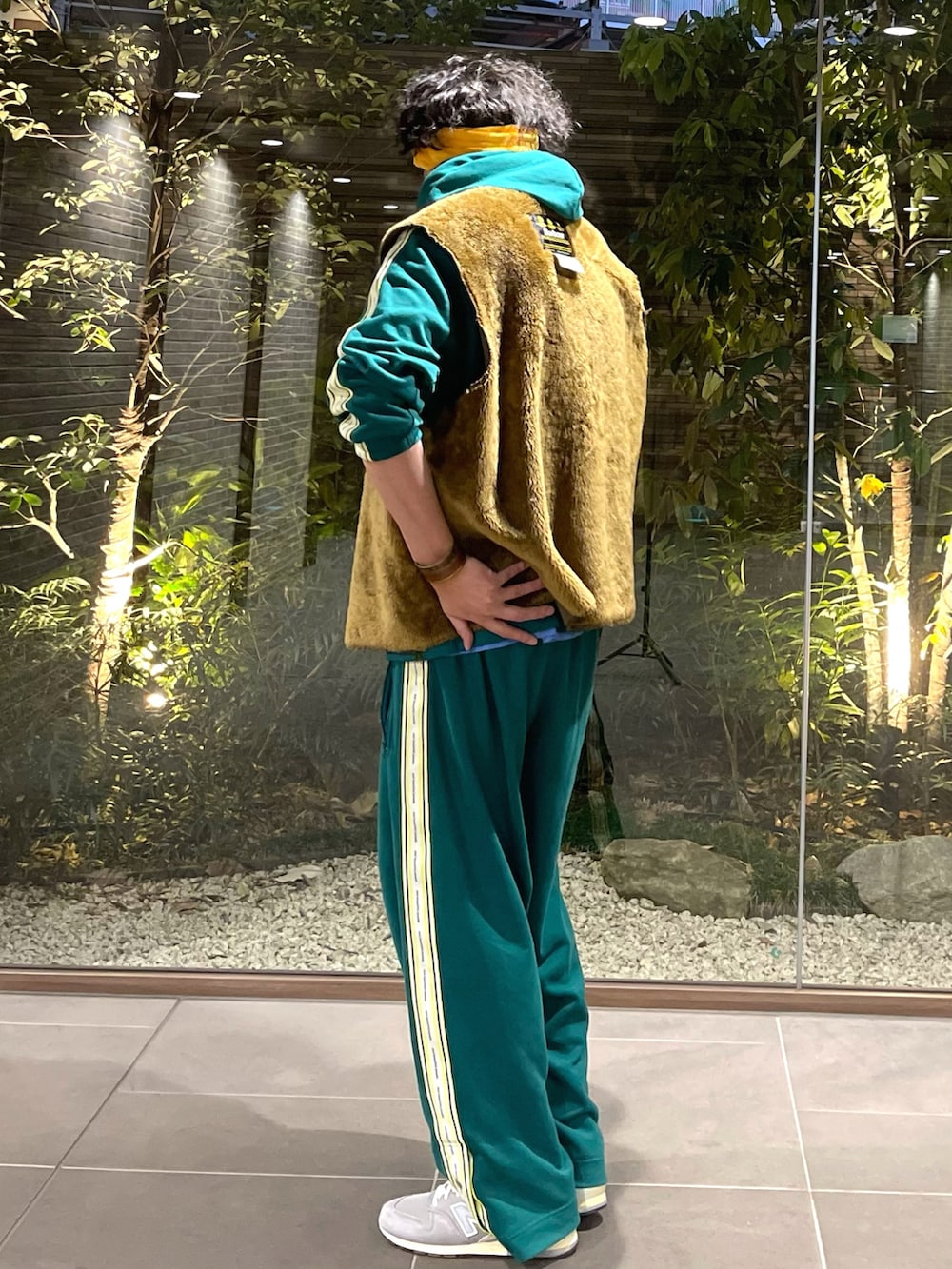 グリーン系のパーカー、ブラウン系のベスト、グリーン系のパンツを着用したメンズの春コーディネートの2枚目の写真