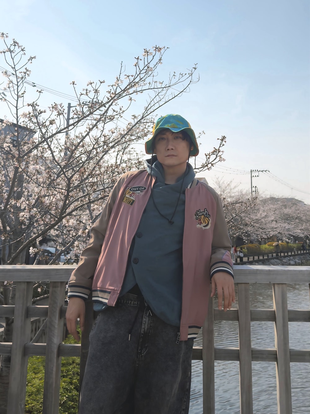 ブラック系のデニムパンツ、ブルー系のカーディガン/ボレロ、ピンク系のスカジャンを着用したメンズの春コーディネートの3枚目の写真