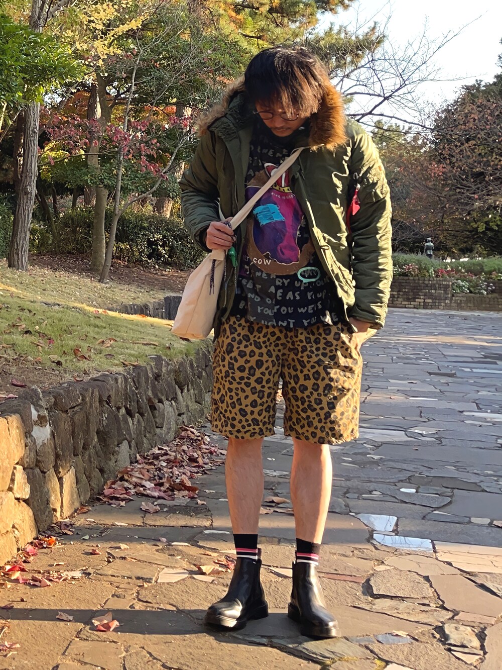 グリーン系のミリタリージャケット、ブラック系のTシャツ/カットソー、ベージュ系のショルダーバッグを着用したメンズの秋コーディネートの2枚目の写真