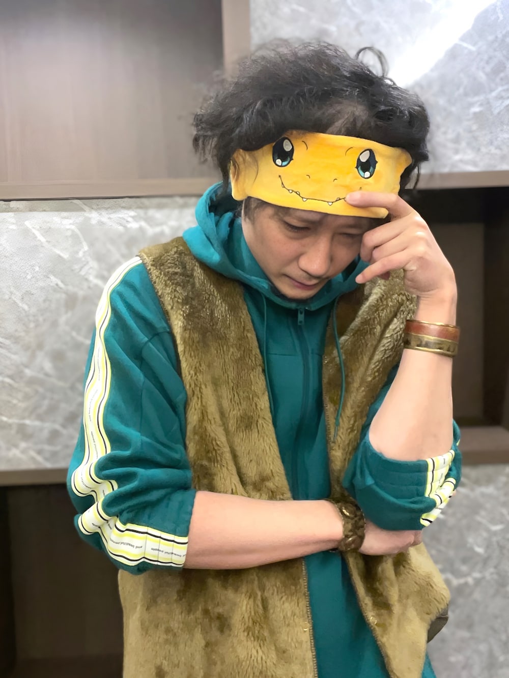 グリーン系のパーカー、ブラウン系のベスト、グリーン系のパンツを着用したメンズの春コーディネートの3枚目の写真