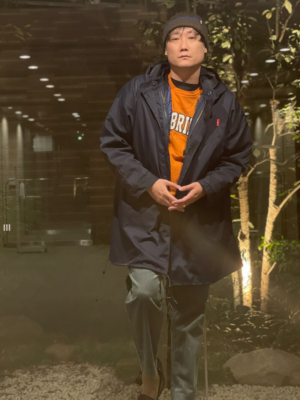 オレンジ系のTシャツ/カットソー、ブルー系のモッズコート、グリーン系のその他パンツを着用したメンズの春コーディネートの2枚目の写真