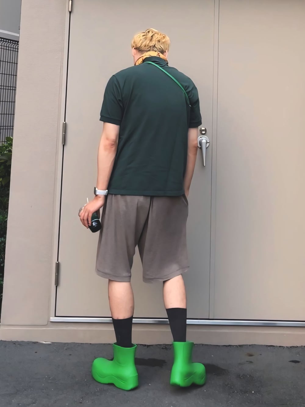 グリーン系のポロシャツ、グリーン系のレインシューズ、グリーン系のショルダーバッグを着用したメンズの夏コーディネートの5枚目の写真