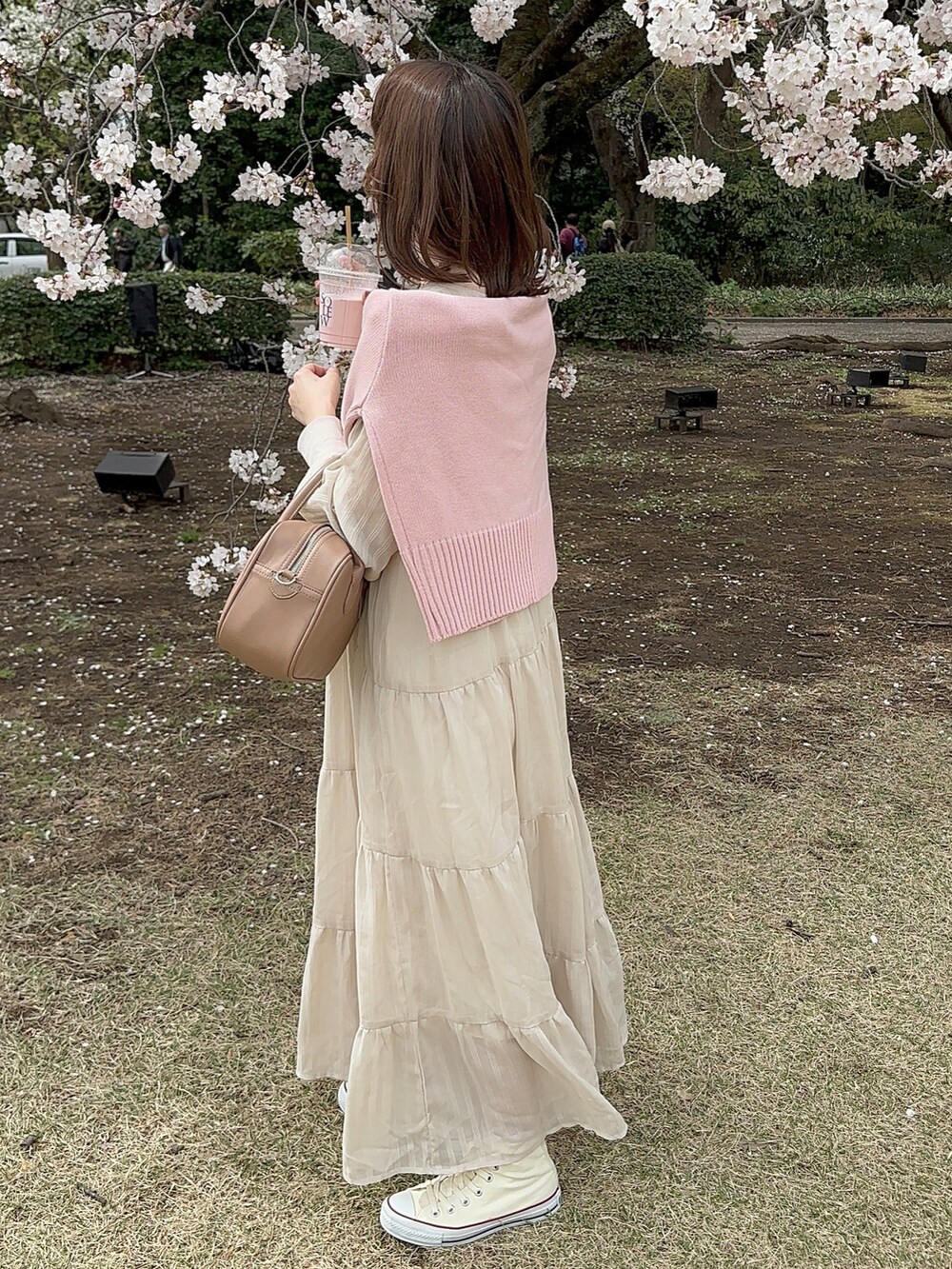 ベージュ系のボストンバッグ、ベージュ系のワンピース、ピンク系のカーディガン/ボレロを着用したレディースの春コーディネートの2枚目の写真