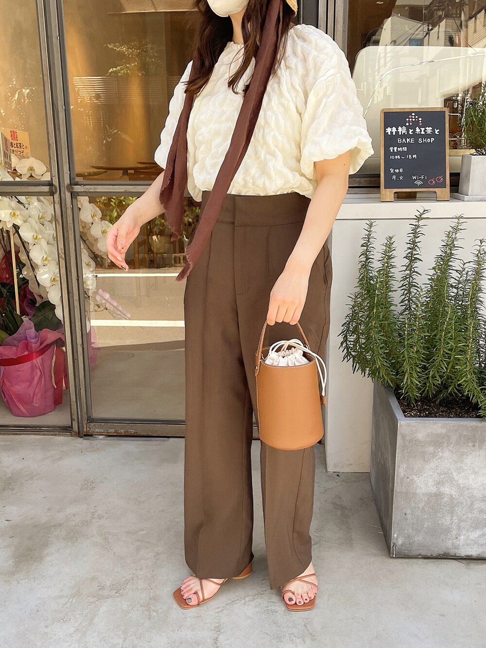 イエロー系のハンドバッグ、ブラウン系のシューズ、ブラウン系のパンツを着用したレディースの夏コーディネートの2枚目の写真