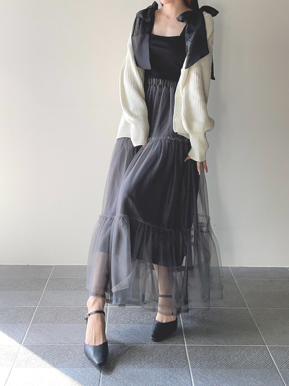 ブラック系のキャミソール、ホワイト系のカーディガン/ボレロ、グレー系のスカートを着用したレディースの冬コーディネートの2枚目の写真