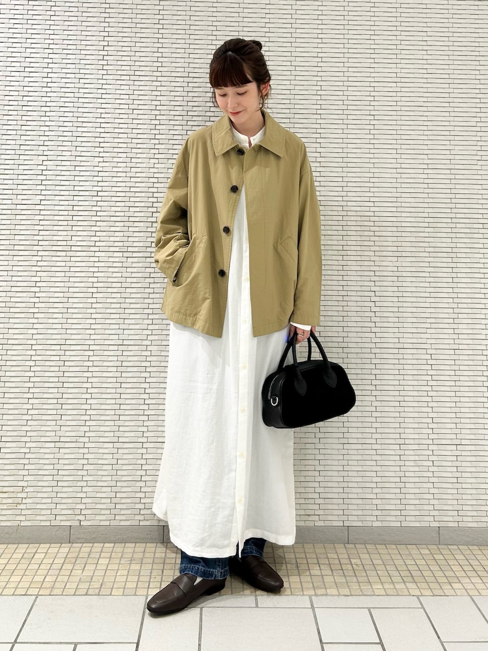 ホワイト系のワンピース、ベージュ系のステンカラーコート、ブルー系のデニムパンツを着用したレディースの秋コーディネートの2枚目の写真