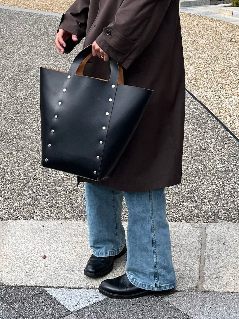 ブラック系のハンドバッグ、ブラック系のブーツ、ブルー系のデニムパンツを着用したメンズの冬コーディネートの4枚目の写真