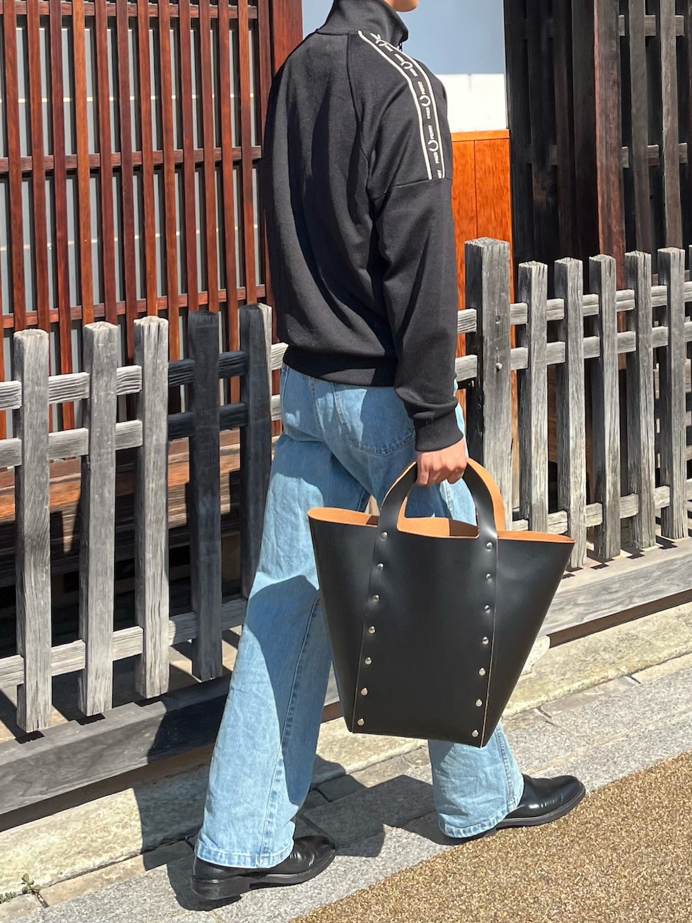 ブラック系のジャージ、ブラック系のハンドバッグ、ブルー系のデニムパンツを着用したメンズの秋コーディネートの2枚目の写真