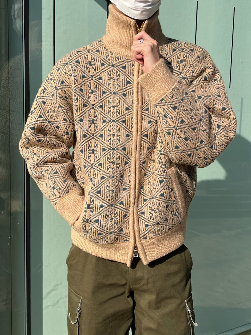 グリーン系のカーゴパンツ、ブラック系のブーツ、ベージュ系のニット/セーターを着用したメンズの冬コーディネートの2枚目の写真