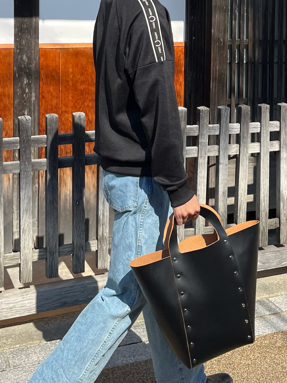 ブラック系のジャージ、ブラック系のハンドバッグ、ブルー系のデニムパンツを着用したメンズの秋コーディネートの4枚目の写真