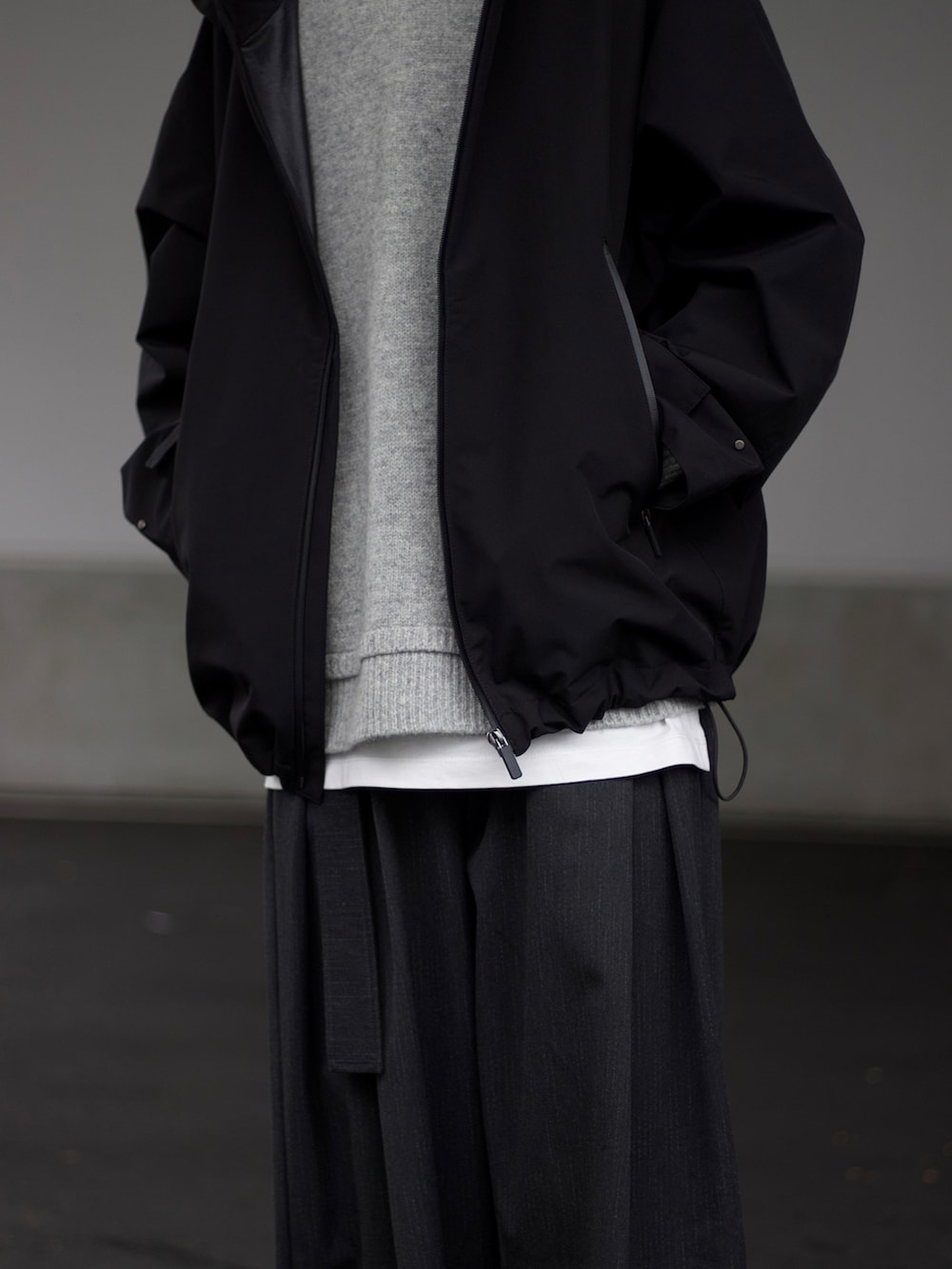 ブラック系のマウンテンパーカー、ベージュ系のニット/セーター、ホワイト系のタンクトップを着用したメンズの秋コーディネートの4枚目の写真